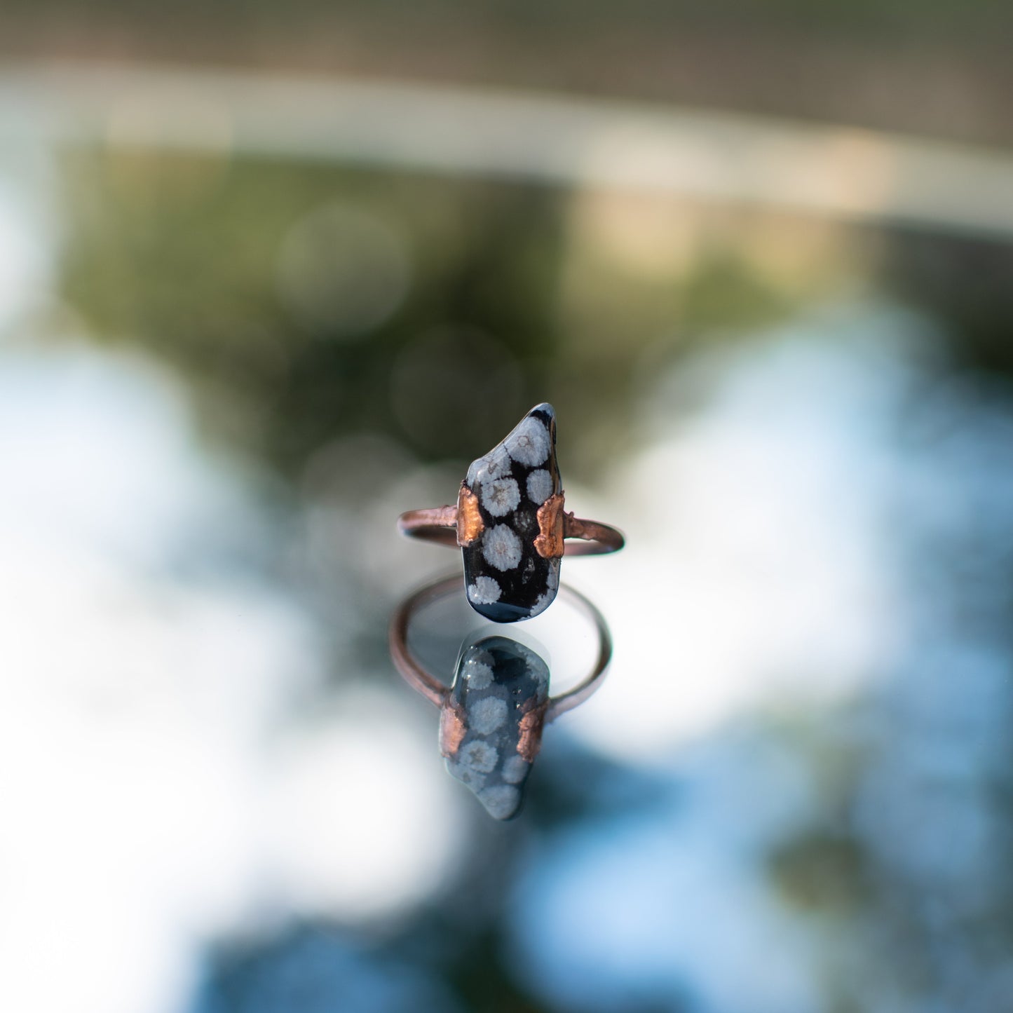 Ring with snowflake obsidian with a blurred background.