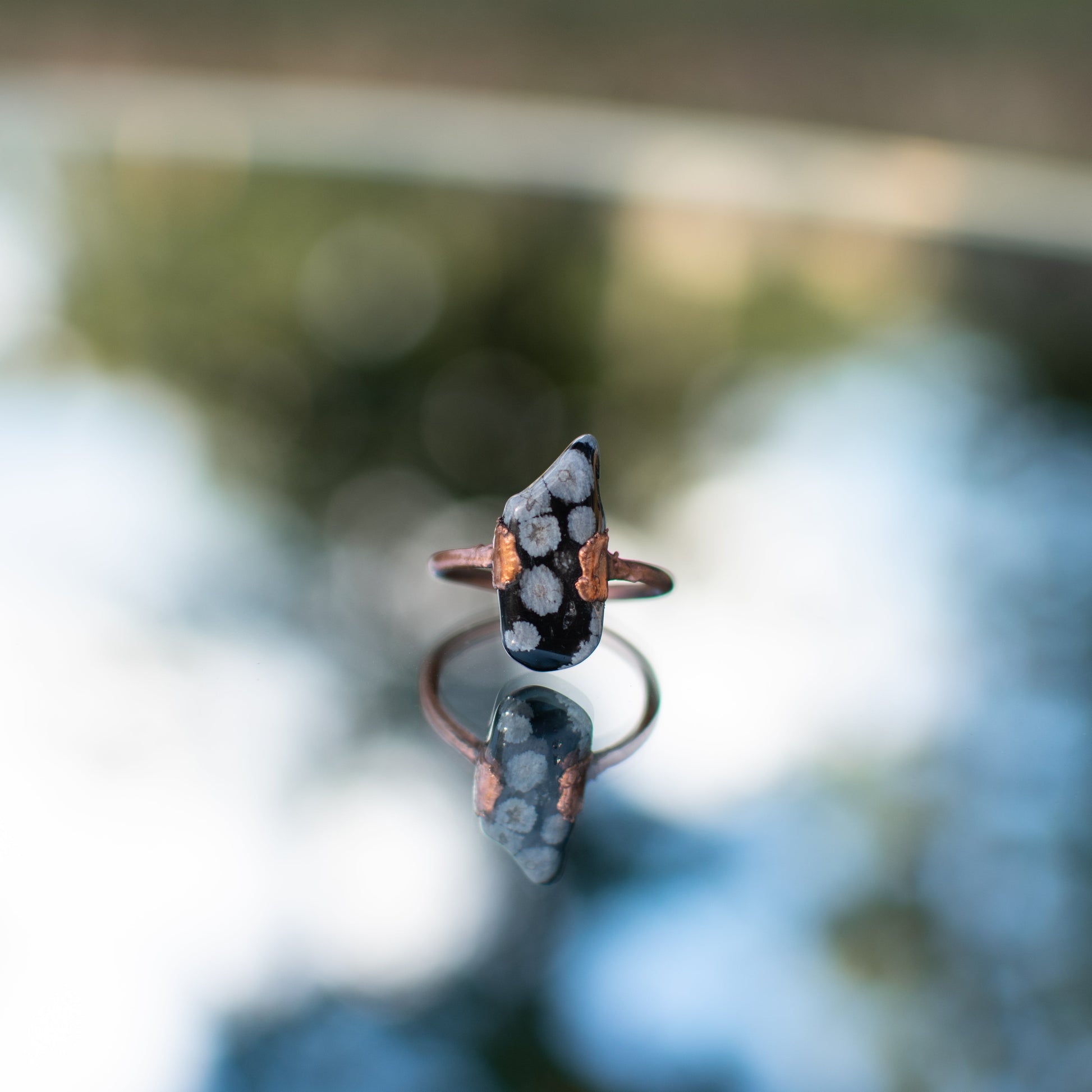 Ring with snowflake obsidian with a blurred background.